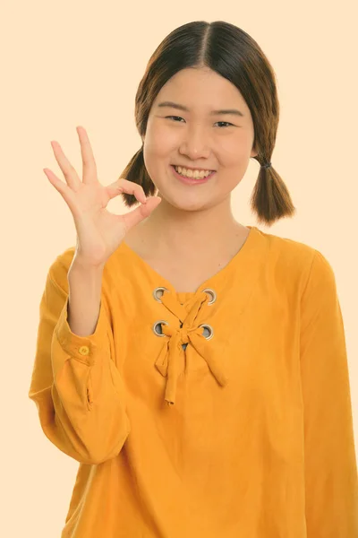 Studio shot de joven feliz mujer asiática sonriendo mientras que da señal ok —  Fotos de Stock