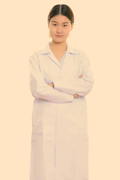 Studio shot de jeune belle asiatique femme médecin debout avec les bras croisés — Photo