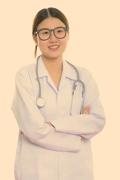 Studio plan de jeune femme asiatique heureuse médecin souriant et pensant avec les bras croisés — Photo