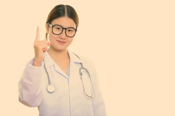 Studio shot de jeune belle asiatique femme médecin pointant doigt vers le haut — Photo