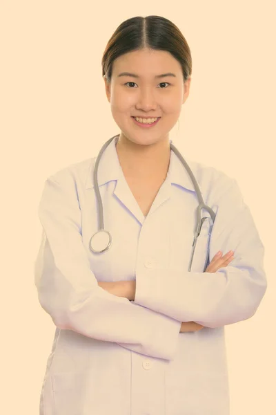 Studio plan de jeune femme asiatique heureuse médecin souriant avec les bras croisés — Photo