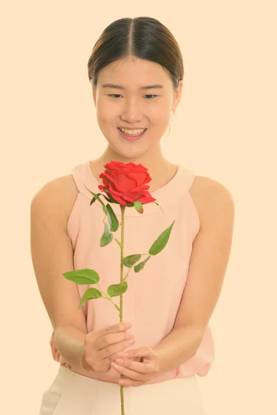 Studio zdjęcie młodej szczęśliwej Azjatki uśmiechniętej i trzymającej czerwoną różę — Zdjęcie stockowe