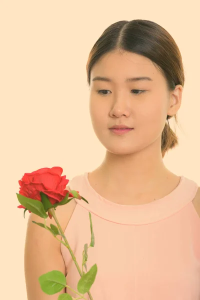 Zbliżenie w górę w górę w młody piękny Azji kobieta gospodarstwa i patrząc w czerwony róża — Zdjęcie stockowe