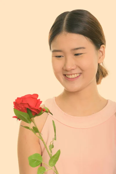 Zbliżenie na młodą szczęśliwą Azjatkę uśmiechniętą trzymając i patrząc na czerwoną różę — Zdjęcie stockowe