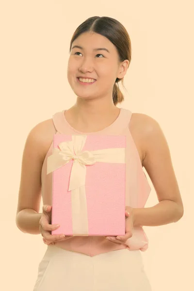 Przemyślana młoda szczęśliwa Azjatka uśmiechnięta i trzymająca pudełko prezentów — Zdjęcie stockowe