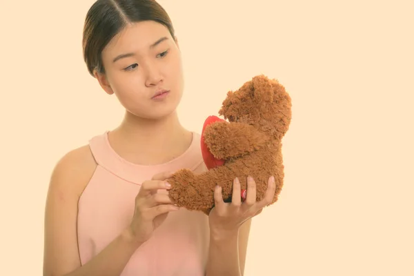 Young beautiful Asian woman holding and looking at teddy bear with heart and love sign — Stock Photo, Image