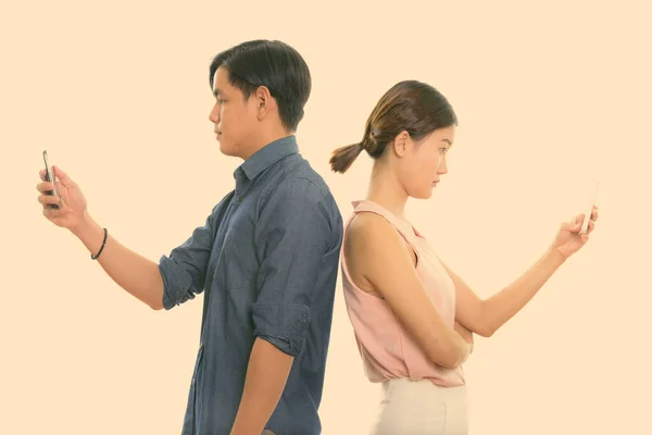 Погляд на молоду азіатську пару за допомогою мобільного телефону, спини одне проти одного. — стокове фото