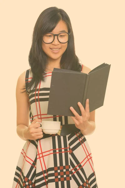 Giovane felice donna d'affari asiatica libro di lettura, mentre tenendo tazza di caffè — Foto Stock