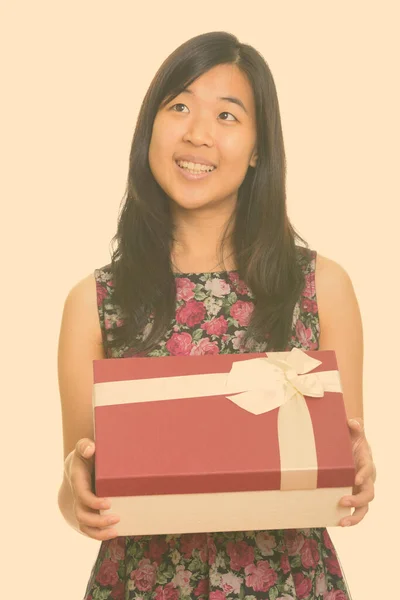Молодая счастливая азиатка держит подарочную коробку, думая: — стоковое фото