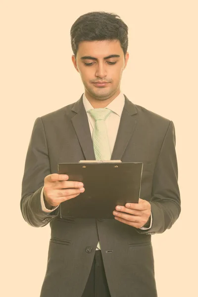 Portret van jonge knappe Perzische zakenman in pak lezen op klembord — Stockfoto