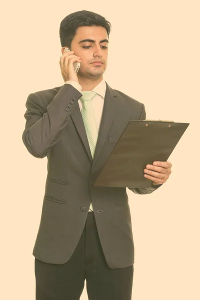 Молодой красивый персидский бизнесмен разговаривает по мобильному телефону, держа планшет — стоковое фото