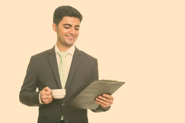 Jong gelukkig Perzisch zakenman het lezen van klembord terwijl het houden van koffie kopje — Stockfoto