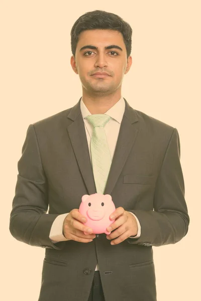 Young handsome Persian businessman holding piggy bank — Stock Photo, Image