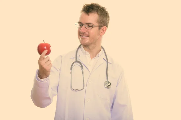 Studio strzał szczęśliwy człowiek lekarz uśmiecha się trzymając i patrząc na czerwone jabłko — Zdjęcie stockowe