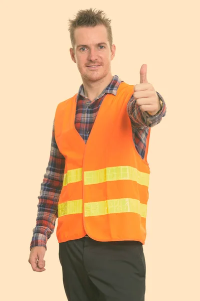 Studioaufnahme eines glücklichen Bauarbeiters, der lächelt, während er den Daumen hebt — Stockfoto