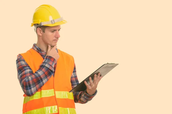 Estúdio tiro de homem trabalhador da construção leitura na área de transferência enquanto pensa — Fotografia de Stock