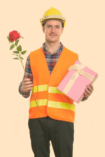 Glücklicher Mann Bauarbeiter lächelt, während er rote Rose und Geschenkbox für den Valentinstag bereit hält — Stockfoto