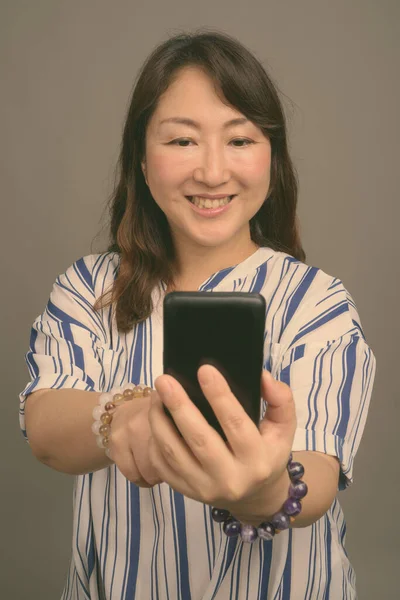 Zralý krásný asijské businesswoman proti šedé pozadí — Stock fotografie