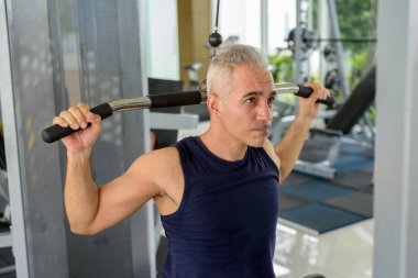 Olgun yakışıklı İranlı adam spor salonunda çekme makinesi kullanıyor.