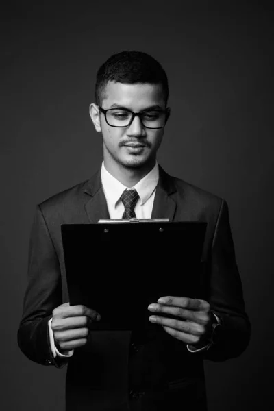 Ung multietnisk asiatisk affärsman i kostym mot grå bakgrund — Stockfoto
