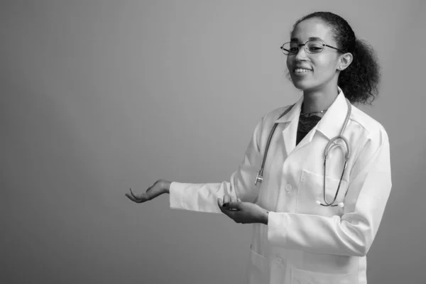 Young beautiful African woman doctor against gray background
