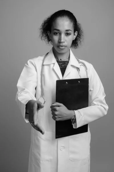 Young beautiful African woman doctor against gray background