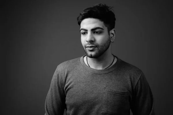 Young handsome bearded Indian man against gray background