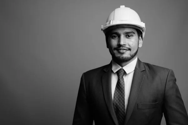 Young handsome bearded Persian businessman wearing hardhat against gray background — Stock Photo, Image