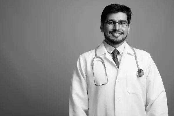 Young handsome bearded Persian man doctor against gray background — Stock Photo, Image