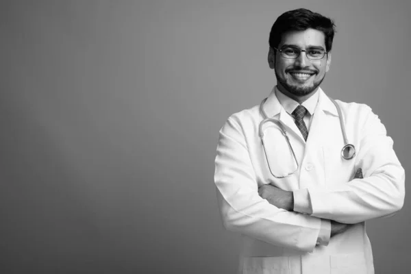 Mladý pohledný vousatý perský muž lékař proti šedé pozadí — Stock fotografie