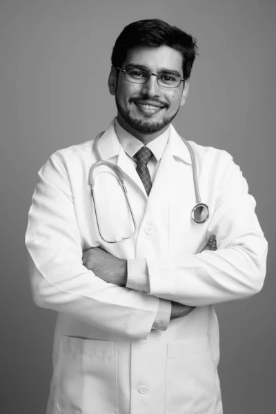 Mladý pohledný vousatý perský muž lékař proti šedé pozadí — Stock fotografie