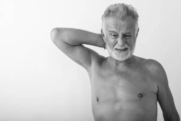 Студійний знімок красивого старшого бородатого чоловіка, який має біль в шиї, без сорочки на білому тлі — стокове фото