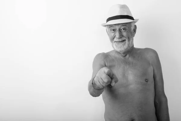 Studio colpo di felice anziano barbuto uomo sorridente mentre indica la fotocamera e indossa cappello senza maglietta contro sfondo bianco — Foto Stock