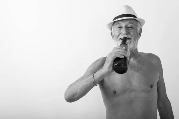 Studio colpo di felice anziano barbuto uomo sorridente mentre beve bottiglia di birra e indossa cappello senza maglietta su sfondo bianco — Foto Stock