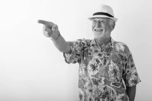 Stúdió lövés boldog idős szakállas turista mosolyog, miközben rámutatott a távolságot, miközben visel kalap ellen fehér háttér — Stock Fotó