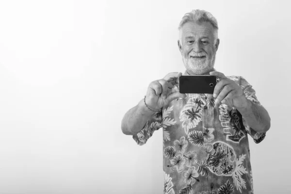 Stúdió lövés boldog idős szakállas turista férfi mosolygós, miközben a kép a mobiltelefon fehér háttér — Stock Fotó