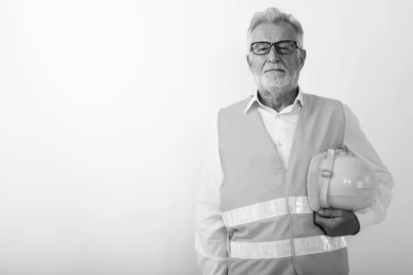 Studio colpo di bello anziano barbuto lavoratore edile tenendo duro cappello mentre indossa occhiali contro sfondo bianco — Foto Stock