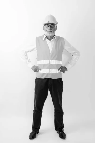 Full body shot di bello anziano barbuto lavoratore edile in piedi con le mani sui fianchi mentre indossa occhiali su sfondo bianco — Foto Stock