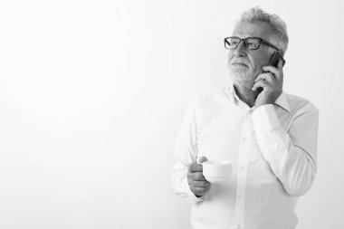 Gözlüklü bir kahve bardağını beyaz arka planda tutarken düşünen ve konuşan yakışıklı yaşlı sakallı adamın stüdyo fotoğrafı.