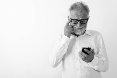 Kafasını beyaz arka planda kaşırken cep telefonu kullanan üzgün yaşlı sakallı adamın stüdyo fotoğrafı.
