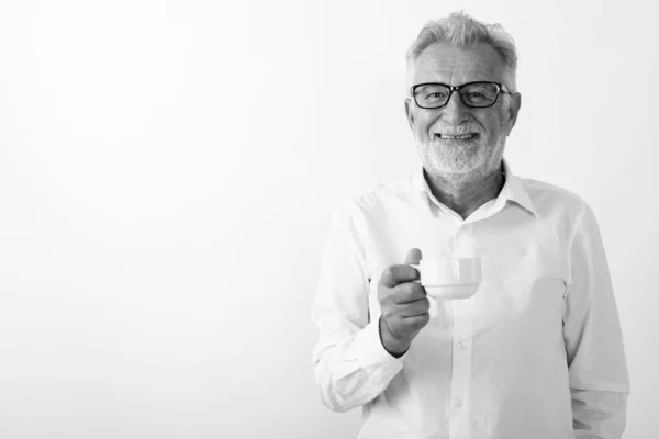 Studio colpo di felice anziano barbuto uomo sorridente mentre tenendo tazza di caffè con occhiali su sfondo bianco — Foto Stock