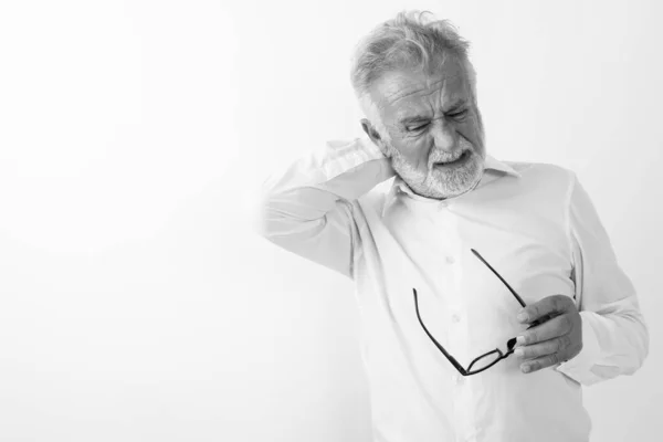 Studio záběr stresu senior vousatý muž s bolestí krku při držení brýlí proti bílému pozadí — Stock fotografie
