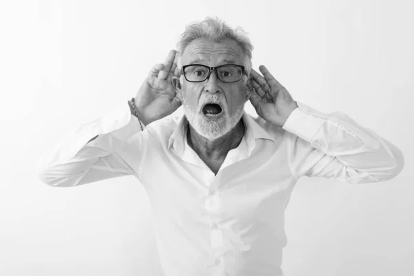 Στούντιο πλάνο του όμορφος ανώτερος γενειοφόρος άνδρας ακούει με τα δύο χέρια στα αυτιά, ενώ φοράει γυαλιά ηλίου σε λευκό φόντο — Φωτογραφία Αρχείου
