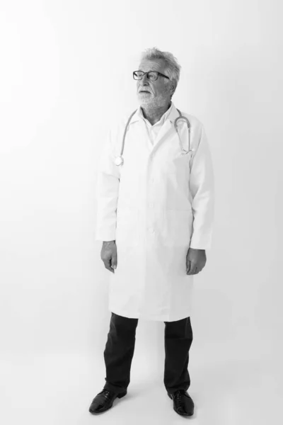 Pieno colpo corpo di bello anziano barbuto uomo medico in piedi e pensare contro sfondo bianco — Foto Stock