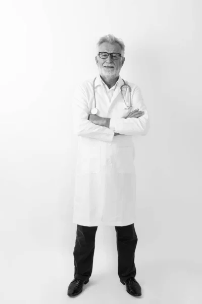 Full body shot di felice anziano barbuto uomo medico sorridente mentre in piedi con le braccia incrociate sullo sfondo bianco — Foto Stock