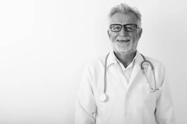 Studio colpo di felice anziano barbuto uomo medico sorridente mentre indossa occhiali contro sfondo bianco — Foto Stock