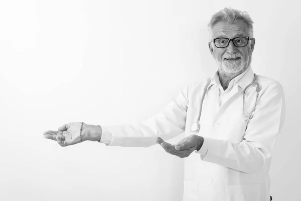 스튜디오는 하얀 배경에 대해 뭔가를보여 주면서 웃고 있는 행복 한 노인 의사의 사진을 찍었다 — 스톡 사진
