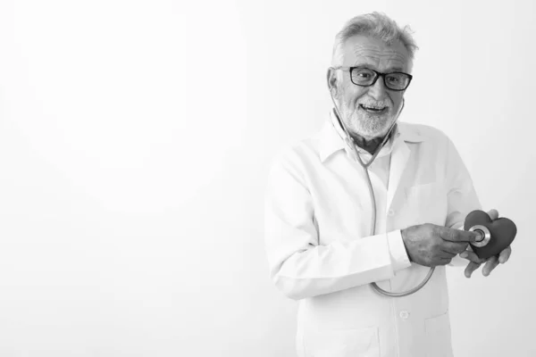 Studio colpo di felice anziano barbuto uomo medico sorridente durante l'utilizzo stetoscopio sul cuore su sfondo bianco — Foto Stock