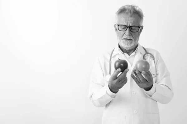 Studio colpo di bello anziano barbuto uomo medico scegliendo tra due mele contro sfondo bianco — Foto Stock