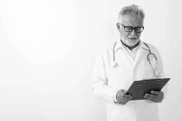 Студійний знімок красивого старшого бородатого лікаря, який читає на кишені на білому тлі — стокове фото